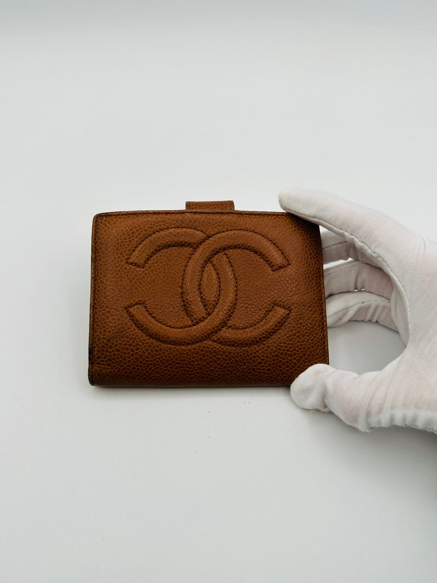 A Chanel Caviar Leather CC Wallet held in a white gloved hand against a white background.
