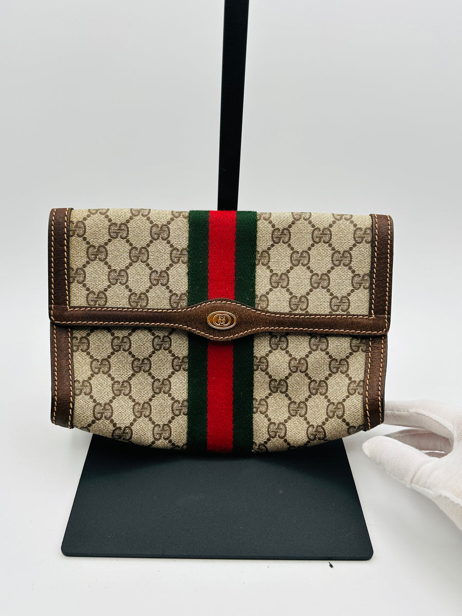 A Gucci vintage clutch bag with a beige and multicolor pattern, featuring a green and red stripe on the front, displayed on a stand.