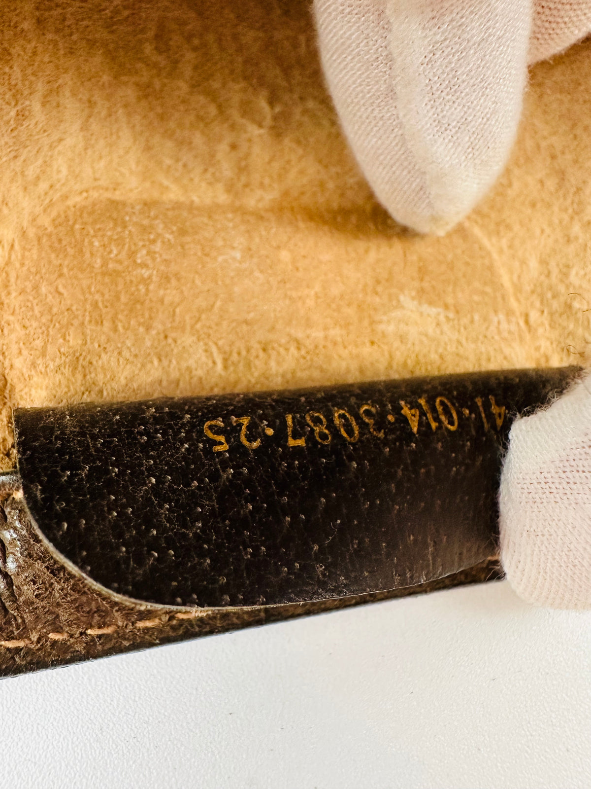 Close-up of a gold serial number stamp on the leather tab of a vintage Gucci clutch, checked during authentication